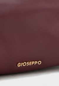 Sac en simili cuir bourgogne avec une texture lisse et un logo doré "Gioseppo" en accent. Forme rectangulaire au design minimaliste.