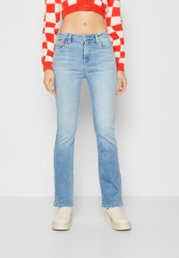 Ljusblå utsvängda jeans i denim, med medelhög midja och femfickorsdesign, kombineras med en röd och vit rutmönstrad kortärmad tröja.