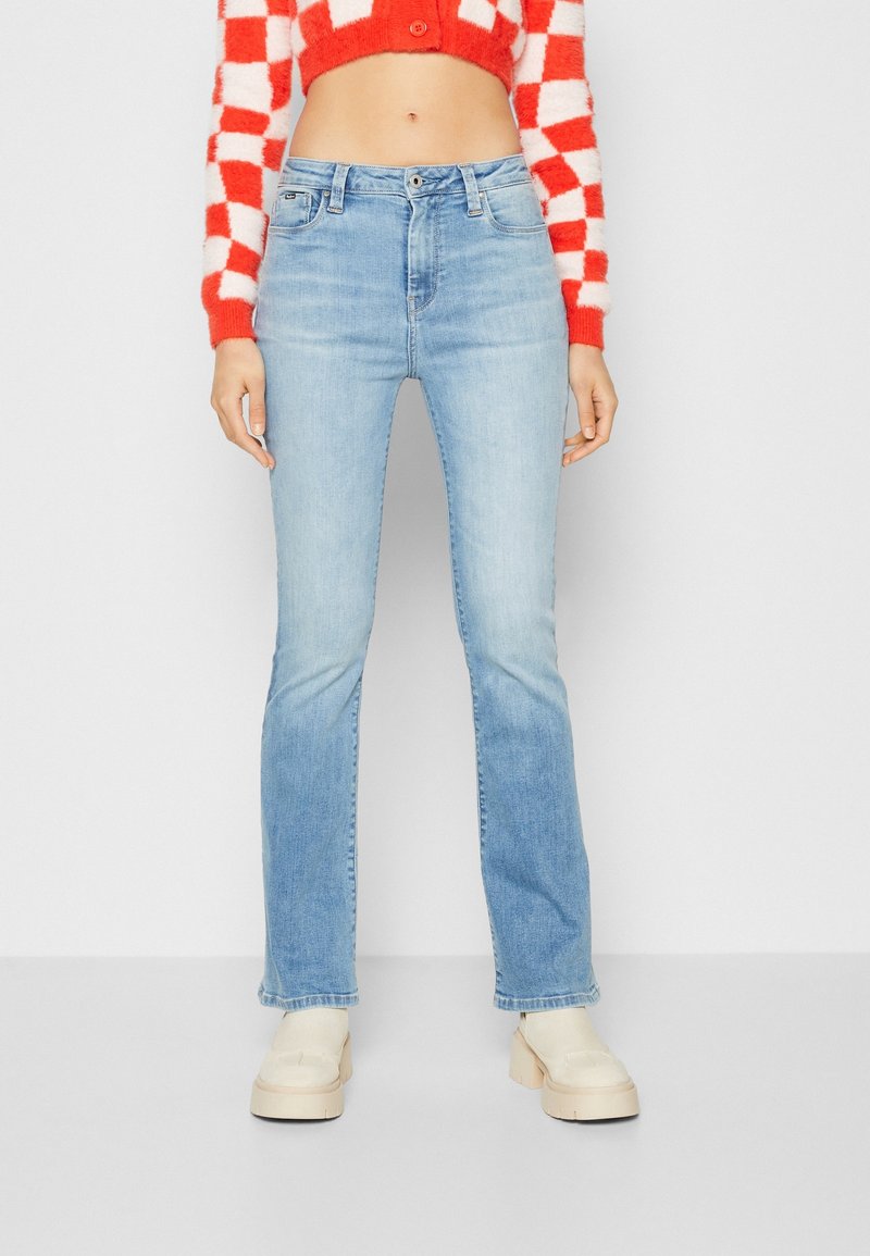 Ljusblå utsvängda jeans i denim, med medelhög midja och femfickorsdesign, kombineras med en röd och vit rutmönstrad kortärmad tröja.