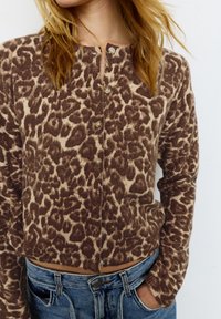 Brązowy i beżowy kardigan w panterkę z guzikami, prążkowaną fakturą, krótkim krojem i długimi rękawami. Nosi się go na jeansy z wysokim stanem.