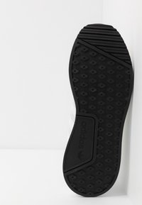 Mustapohjainen kumipohja, jossa on kuvioitu geometrinen kuvio. Valkoinen päällinen, jossa on kolme kapeaa raitaa ja logodetalji.