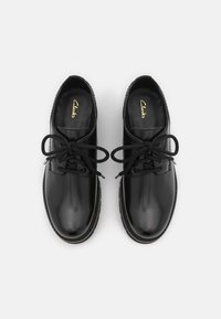 Chaussures en cuir noir avec bouts ronds, design à lacets, texture lisse et léger brillant. Présente un intérieur confortable et une semelle cousue.