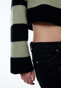 Gebreid cropped sweater in afwisselende groene en zwarte strepen, met een geribbelde zwarte zoom. Slanke zwarte jeans met een zichtbaar pocketdetail.