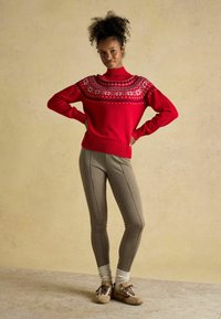 Punane kudumislõngast kampsun, millel on fair isle muster ja kõrge kaelus; kombineeritud sobivate houndstooth pükstega ning beežide tennisetossudega, millel on pruunid aktsendid.