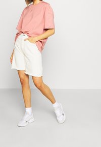 Ljusrosa oversized t-shirt med korta ärmar, prydd med tre sidostråk, matchad med vita denimshorts med rå kant. Vita sneakers.