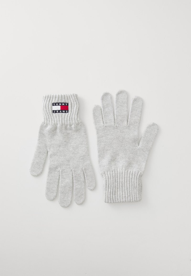 Sivé pletené rukavice s rebrovanými manžetami, na ktorých je štítok s logom "TOMMY JEANS" v čiernej, červenej a bielej farbe. Hladká textura, štandardný dizajn s piatimi prstami.