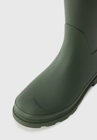 Green rubber boot featuring a smooth finish, rounded toe, textured sole, and a seam detail on the upper part.
