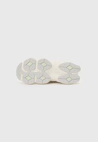 Semelle de sneaker blanche avec un fond en caoutchouc texturé. Présente des accents verts hexagonaux et une semelle à motif pour une meilleure adhérence. Design simple et minimaliste.