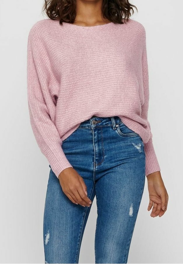 Hellrosa gestrickter Pullover mit lockerem Sitz, langen Ärmeln und geripptem Muster, kombiniert mit dunkelblauen Skinny-Jeans mit ausgewaschenen Details.