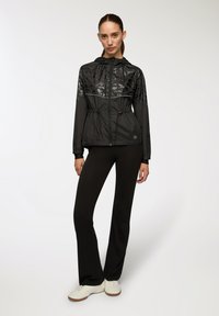 Czarna lekka kurtka z błyszczącymi akcentami, wiązaniem w talii, kapturem i zapięciem na zamek błyskawiczny. Połączona z czarnymi spodniami dzwonami i białymi sneakersami.