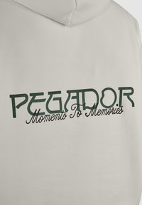 Sweat à capuche blanc avec texte vert foncé "PEGADOR" et texte noir en cursive en dessous indiquant "Moments To Memories" dans le dos.