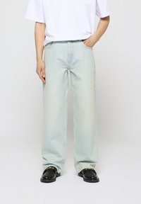 Jeans azzurri chiari a gamba larga con una finitura sbiadita, caratterizzati da un classico modello a cinque tasche. Indossati con una t-shirt bianca semplice e scarpe nere.