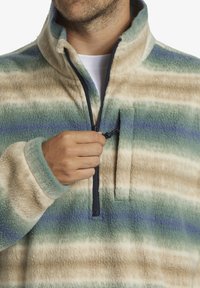 Pullover en polaire à fermeture quart de zip dans un motif rayé beige, vert et bleu. Texture douce avec un col montant et un détail de poche poitrine zippée.