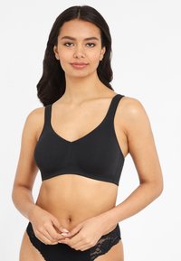 Svart trådlös behå med V-ringad design, tillverkad av mjukt stretchmaterial. Har breda axelband och minimalistisk sömnad för komfort.