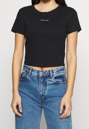 Camiseta negra corta con mangas cortas, escote redondo y logo en blanco "CALVIN KLEIN JEANS" en la parte frontal. Combinada con unos jeans azul de cintura alta.