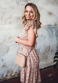 Šaty s květinovým vzorem v krémové barvě s růžovými a červenými květinami, s volány na rukávech a s vrstvou na spodním okraji. Je k nim přidána malá béžová kabelka s řetízkovým popruhem.