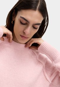 Maglione lavorato a maglia di un delicato rosa chiaro con texture a coste e scollo rotondo, caratterizzato da dettagli di cucitura discreti sulle spalle e maniche lunghe.