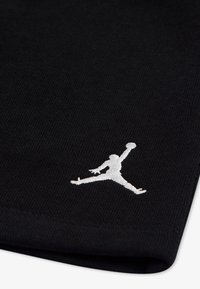 Schwarzer Stoff mit gerippter Textur; verfügt über ein weiß gesticktes Jumpman-Logo. Der Rand ist sauber gesäumt.