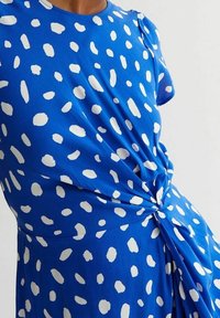 Abito blu con motivo a pois bianchi, scollatura rotonda, maniche corte e dettaglio intrecciato in vita. Tessuto morbido, design casual.