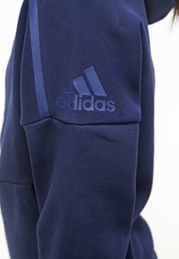 Mörkblå sweatshirt med texturerad tyg, med en upphöjd Adidas-logotyp på axeln och ett slätt accentband.