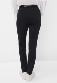 Schwarze, enganliegende Hosen aus glattem Stoff mit schlanker Silhouette, hoher Taille und einem dünnen schwarzen Gürtel, kombiniert mit weißen Sneakers.
