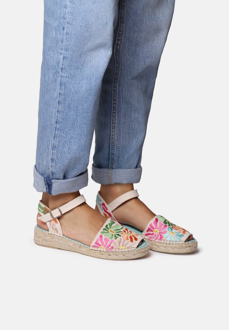 Väriküllased tikitud espadrilled, millel on naturaalsest jute-st valmistatud tallad, suletud varba ja pahkluupannal. Need on kombineeritud üles keeratud teksadega.