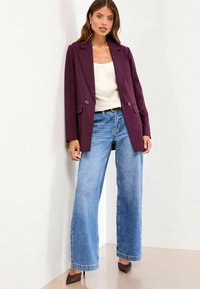Burgunderfarvet skræddersyet blazer med ndre slag, parret med lyseblå denimbukser med bred ben. Sættet komplementeres af brune højhælede sko.