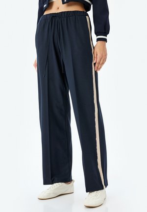 Pantalones de chándal azul marino con cintura ajustable mediante cordón, que cuentan con una franja lateral beige. Fabricados con un tejido suave y elástico para mayor comodidad.