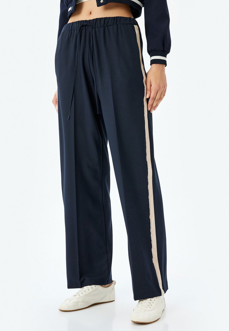 Marineblauwe trainingsbroek met een touwtjes taille, voorzien van een beige zijstreep. Gemaakt van een zachte, elastische stof voor comfort.