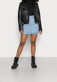 Veste de moto en cuir noir, col roulé noir, mini-jupe en denim bleu clair avec des boutons, et bottines noires à boucle avec semelle texturée.