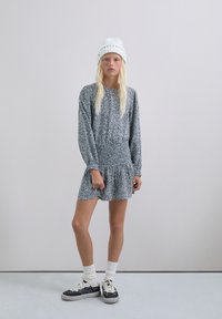 Vestido a rayas en blanco y negro con mangas largas y cintura fruncida; combinado con zapatillas negras y calcetines blancos; la modelo lleva un gorro de punto blanco.