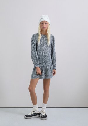 Vestido a rayas en blanco y negro con mangas largas y cintura fruncida; combinado con zapatillas negras y calcetines blancos; la modelo lleva un gorro de punto blanco.