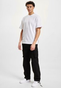White cotton t-shirt with a relaxed fit, paired with black cargo pants featuring side pockets, and white sneakers with black accents.