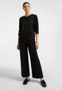 Černý dlouhý rukáv s volným střihem, zkombinovaný s tmavými džínami s vysokým pasem a širokými nohavicemi, a černými mokasínami. Hladká textura a klasický design.