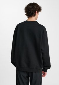 Svart sweatshirt med rund halsringning, neddragna axlar och ribbade ärmslut. Har subtila sömdetaljer längs ärmarna. Mjuk tygtextur.