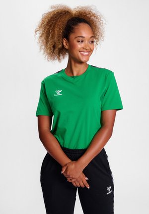 Grøn t-shirt med en blød tekstur, korte ærmer og V-halsdesign. Har sorte accenter på skuldrene og et logo på brystet.