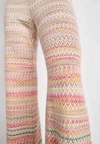 Patterned knit pants featuring a zigzag design in pastel colors, primarily beige, pink, and gold, with a soft texture and wide legs.