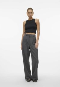 Top corto negro acanalado combinado con pantalones de talle alto gris con pliegues, complementados con zapatos planos de tejido negro. Diseño simple y moderno.