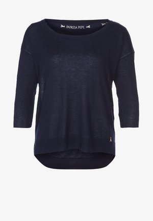 Granatowy, lekki sweter z rękawami do trzy czwarte, okrągłym dekoltem i asymetrycznym dołem. Posiada mały metalowy akcent w postaci logo.