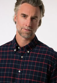 Námořnická modrá kostkovaná košile s červeným a šedým mřížkovým vzorem, s neklesajícím límcem a malými bílými knoflíky. Měkká textilie.