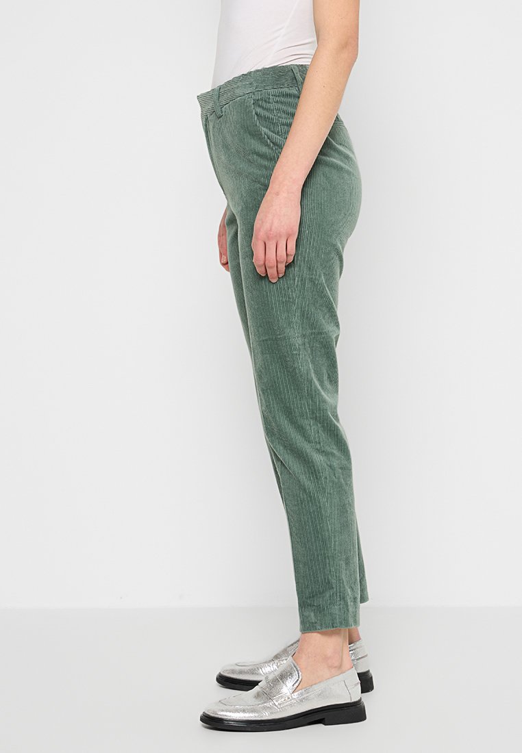 Grüne Cordhosen im Slim Fit, aus strukturiertem Material, mit flachem Bund und Seitentaschen, getragen mit silbernen, metallischen Slippern.