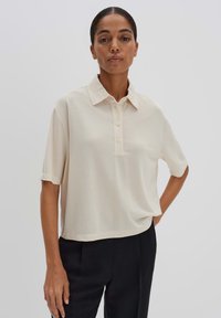 Polo à manches courtes en beige clair, avec un col, une patte de boutonnage à trois boutons et une coupe décontractée avec une texture douce.