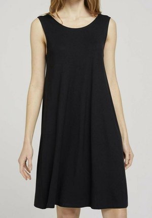 Bezrekawowa czarna sukienka w kształcie litery A noszona przez osobę, sięgająca powyżej kolan, z okrągłym dekoltem.