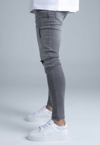 Szürke skinny farmer szakadt részletekkel és fehér platform tornacipő perforált díszítéssel és fűzővel.