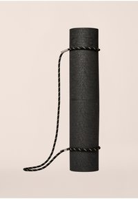 Μαύρο υφασμάτινο στρώμα γιόγκα τυλιγμένο κατακόρυφα, ασφαλισμένο με έναν πλεγμένο μαύρο και χρυσό ιμάντα. Διαθέτει ανάγλυφο λογότυπο στην επάνω πλευρά.