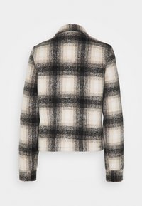 Veste à carreaux dans des nuances de noir, blanc et beige. Présente un col, des manches longues et un tissu texturé mettant en valeur un motif à carreaux.