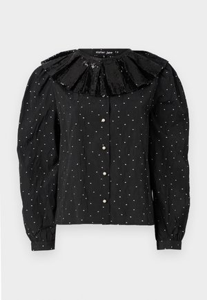 Svart bluse med en paljettbesatt volangkrage, perleknapper og et teksturert stoff med små hvite prikker. Lange puffede ermer fullfører designet.