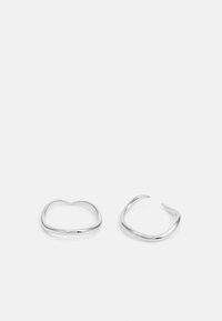 Cercei din metal argintiu cu un design deschis, abstract. Au linii netede, curbe și o formă asimetrică.