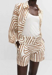 Camicia leggera a righe in beige e marrone con vestibilità rilassata, abbinata a pantaloni corti a vita alta con cintura in vita.