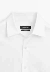 Biała koszula z strukturalnym kołnierzykiem, guzikiem z przodu i gładką fakturą. Posiada czarne metki marki z napisem "Massimo Dutti" oraz "Wyprodukowano w Egipcie".